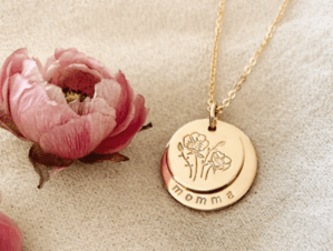 gold disc necklace with word momma on it and flowers, pink flower in background