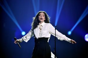 Lorde performs at the 60th Annual GRAMMY Awards wearing a white blouse and black belted skirt with her arms extended out her sides.
