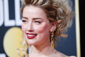 Amber Heard smiling looking left with her hair up wearing red lipstick.