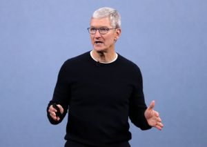 Tim Cook wearing a black crewneck sweater facing left wearing glasses with his arms reaching out.