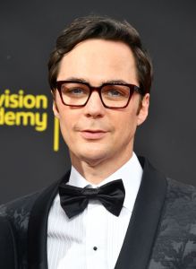 Jim Parsons smirking wearing a suit and bowtie wearing black framed glasses.