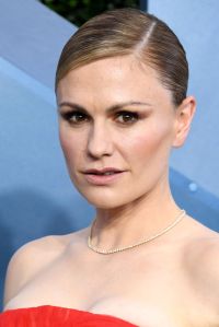 Anna Paquin with her hair slicked back with a deep side part wearing a strapless red dress.