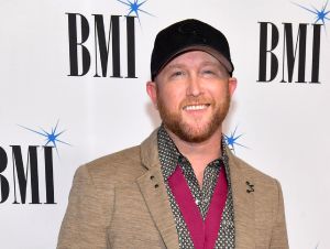 Cole Swindell on the red carpet at the BMI Awards in a brown jacket and black ball cap