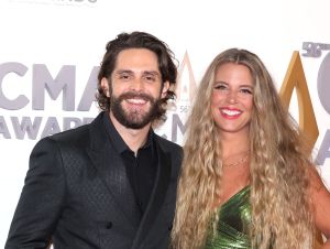 Thomas Rhett in a pattern black blazer and his wife Lauren in a green dress on a CMA Red Carpet