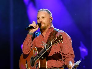 Cody Johnson on stage with a guitar wearing a patterned orange cowboy shirt