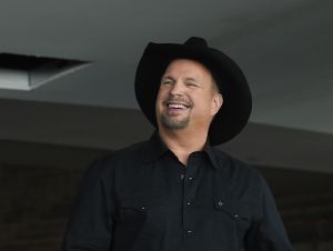 Garth Brooks smiling in a black button down shirt and a black cowboy hat