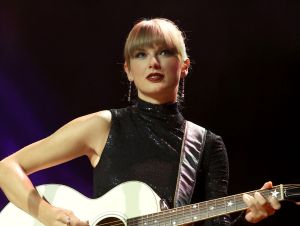 Taylor Swift wearing a black dress on stage holding a guitar