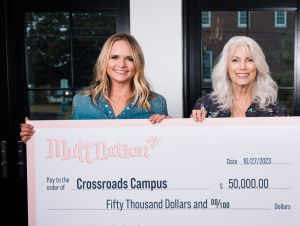 Miranda Lambert in blue and Emmylou Harris in black holding a big check