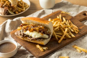Homemade Beef French Dip Sandwich with French Fries served on a cutting board.