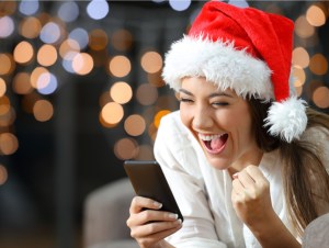 Excited woman reading text on a phone on christmas lying on a couch in the living room at home