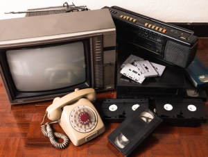 Old telephone and obsolet electronic equipment on wooden floor, outdated tech concept.