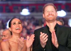 Prince Harry, Duke of Sussex, wearing a black dress shirt smiling and clapping and Meghan, Duchess of Sussex wearing a strapless green dress smiling and clapping attend the closing ceremony of the Invictus Games Düsseldorf 2023