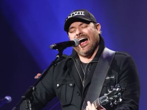 Chris Young performing on stage playing a guitar in a black jacket and ball cap