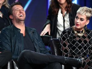 Luke Bryan laughing in a black jacket, with Katy Perry in a gold and black outfit