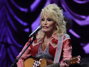 Dolly Parton performing with a guitar in a red patch colored top