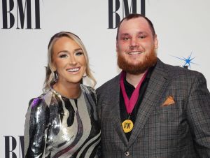 Luke Combs in a brown suit with his wife Nicole in a black and silver dress on a red carpet