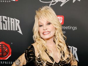 Dolly Parton posing on a red carpet in a black pant suit