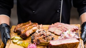 Smoked meat assortment, coleslaw salad, pickles served on a platter with a chef holding the tray.