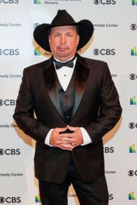 Garth Brooks attends the 43rd Annual Kennedy Center Honors wearing a black suit and bowtie with a black cowboy hat with his hands laced in front.