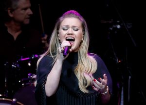 Kelly Clarkson performs onstage for The Final Nashville Show - A Tribute To Ronnie Milsap wearing a black shirt singing holding a microphone with her eyes closed, Kelly Clarkson's Best Kellyoke Performances Of 2024 (So Far).