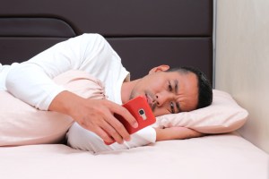 Adult Asian man checking his mobile phone after waking up