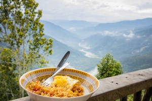 Noodles and an egg served in a bowl for breakfast. Photo taken with background of hills and river valley.