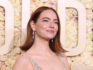 Emma Stone attends the 81st Annual Golden Globe Awards smiling looking up and right wearing a golden gown.