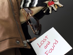 Multiple items (house keys, sunglasses, cotton stripped glove, coat) on a reflective table with a lost and found sign.