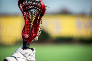 Red lacrosse stick held in a players right hand. With a glove and ball in pocket