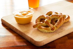 Soft pretzels and dipping cheese on wood cutting board with beer
