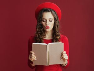 surprised stylish 40 years old woman in red dress and beret isolated on red background with book