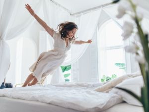Woman jumps on the bed as if in flight.