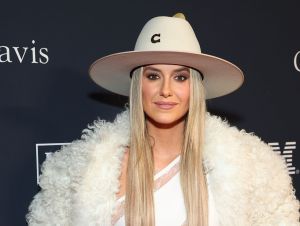 Lainey Wilson in a white fluffy coat and cowboy hat posing on a red carpet.