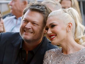 Blake Shelton in a black blazer sitting next to Gwen Stefani in a silver dress.