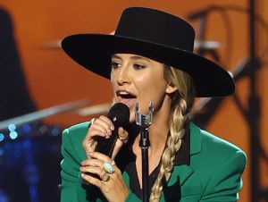 Lainey Wilson performing on stage in a green suit and black hat.