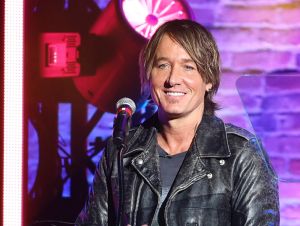 Keith Urban wearing a back leather jacket standing in front of a microphone.
