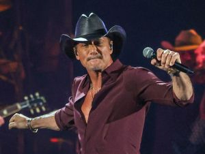 Tim McGraw on stage in a maroon shirt and a black cowboy hat.