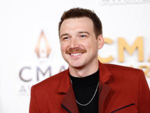 Morgan Wallen posing in a black t-shirt, gold chain and red jacket on a CMA red carpet.