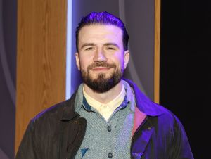 Sam Hunt posing in a black jacket and button-down gray shirt.