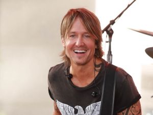 Keith Urban is on stage smiling in a black t-shirt.