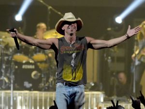 Kenny Chesney on stage wearing a black concert t-shirt and a cowboy hat.