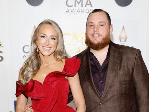 Luke Combs in a brown plaid blazer and his wife Nicole in a red dress on a CMA red carpet