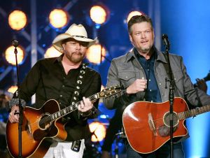 Toby Keith on stage stage with a guitar in a cowboy hat and Blake Shelton on stage with a guitar in a denim jacket