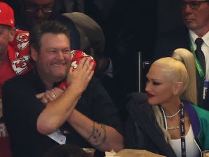Blake Shelton in a black shirt with Gwen Stefani in a white tank top and jacket, sitting in their Super Bowl suite.