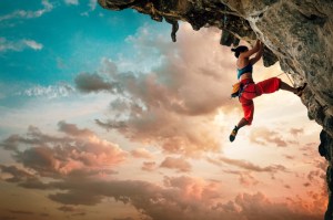 Athletic Woman climbing on overhanging cliff rock with sunset sky background