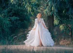 Young woman in incredibly dress with feathers. Creative cloak embroidered with stones, silver and down. White dress with a corset and a long skirt with tulle fluttering in the wind. Art photography