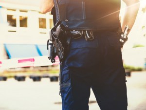 Policeman on crime scene . Red plastic tape and police officer, gun belt, handcuffs and gun.With a sunshine flare coming in.