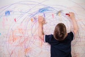 The child draws on the wall with colored chalk. The boy is engaged in creativity at home