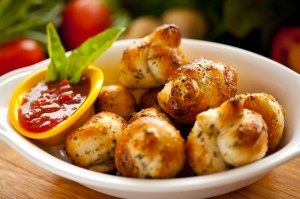 A tight shot on a freshly baked batch of garlic bread knots with a marinara dipping sauce.