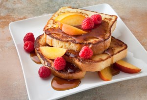 French toast with peach's and raspberries on a marble countertop.